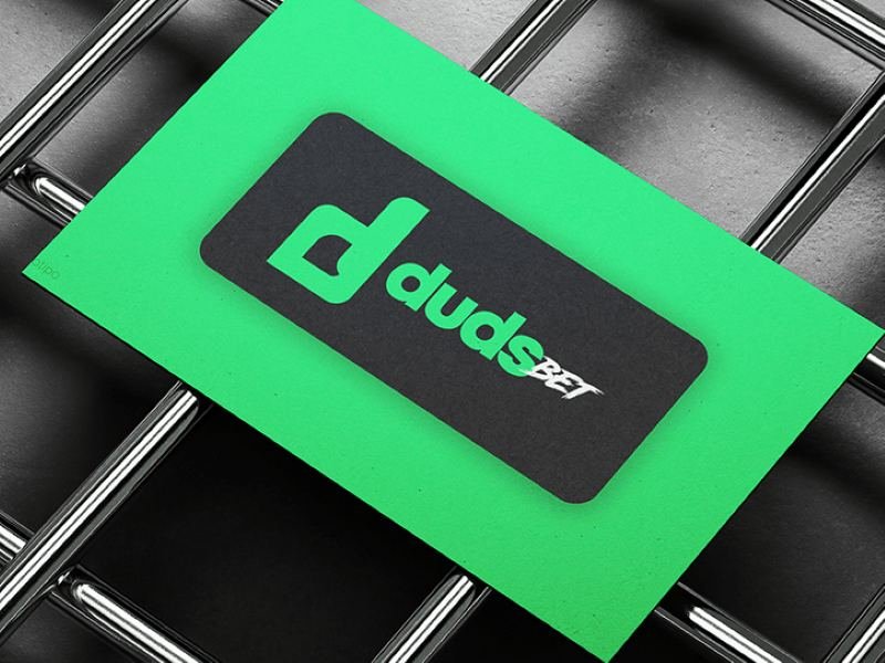 Cartão verde com a marca Duds Bet sobre uma grade metálica